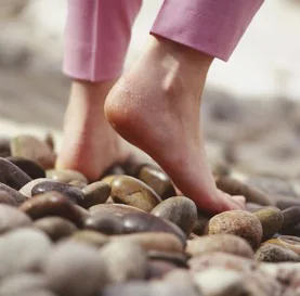 Bare feet in pink pants walking across smooth river stones