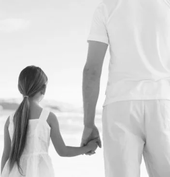 A father and young daughter walking hand in hand toward the shore