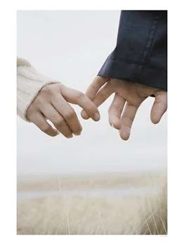 Two hands gently linked by their little fingers in a field