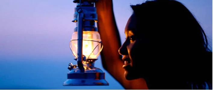A woman holding a lit lantern against an evening sky