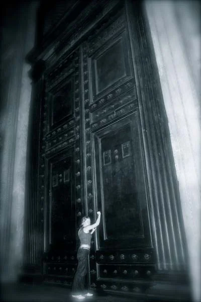 A small figure reaching up at an enormous ancient door