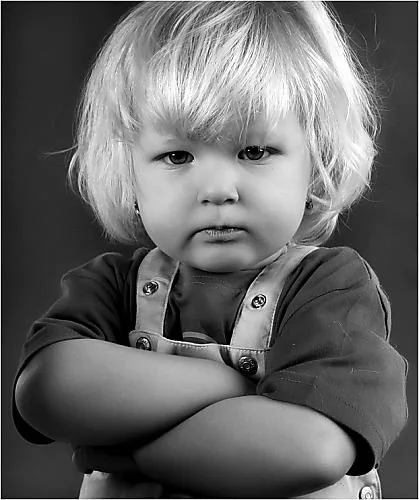 A small child standing with arms crossed and a stubborn expression