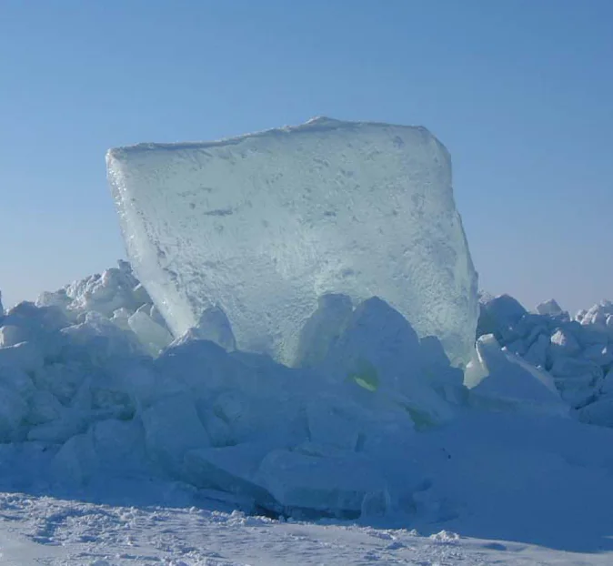 A block of ice glowing in the sunlight on a frozen shoreline