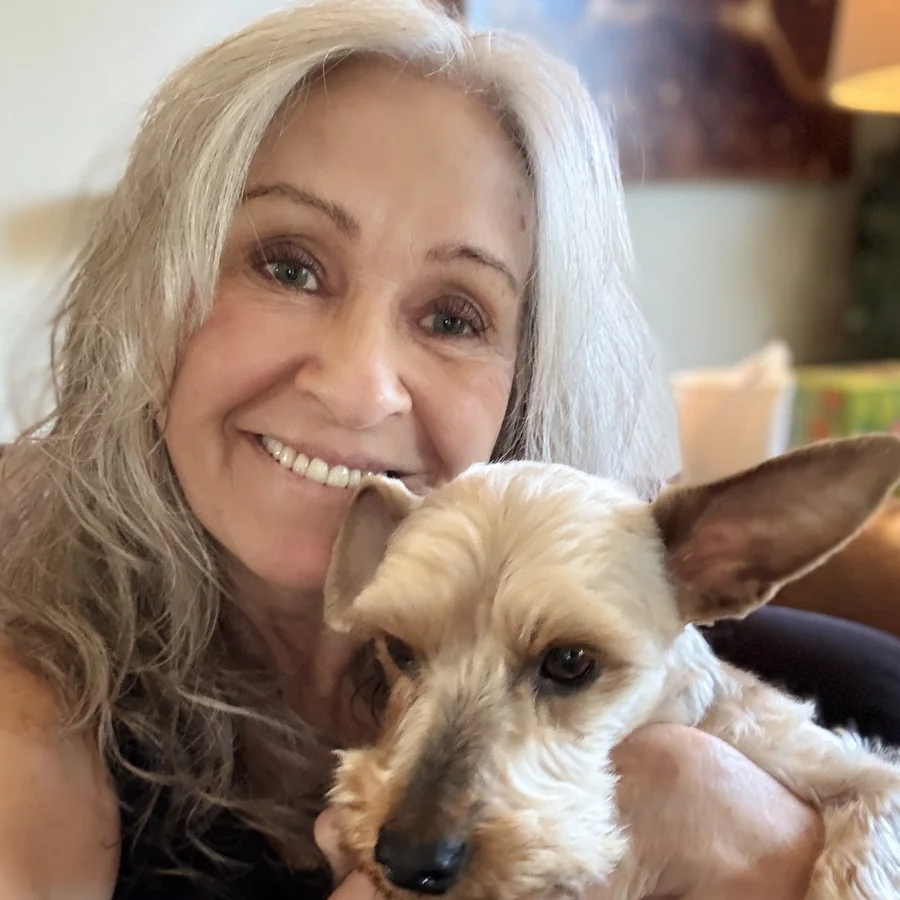 Joanna Mikel smiling with Ari, her little dog, snuggled close